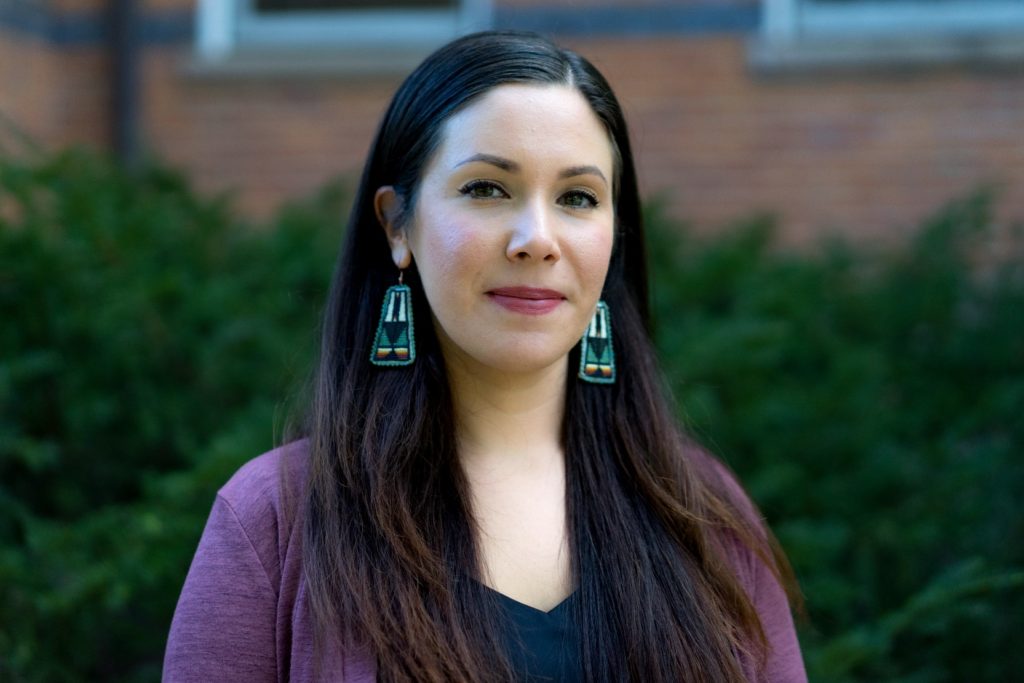 A head and shoulder shot of a woman with long dark hair wearing long dangling earrings. 