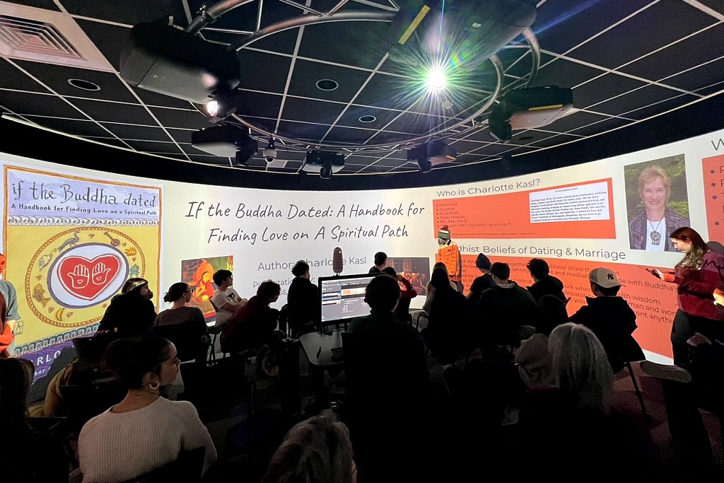 Students sit facing a curved projection screen in a classroom as a student presenter stands at the front discussing "If the Buddha Dated: A Handbook for Finding Love on a Spiritual Path."
