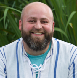 Portrait photo of a bald, bearded man outdoors.