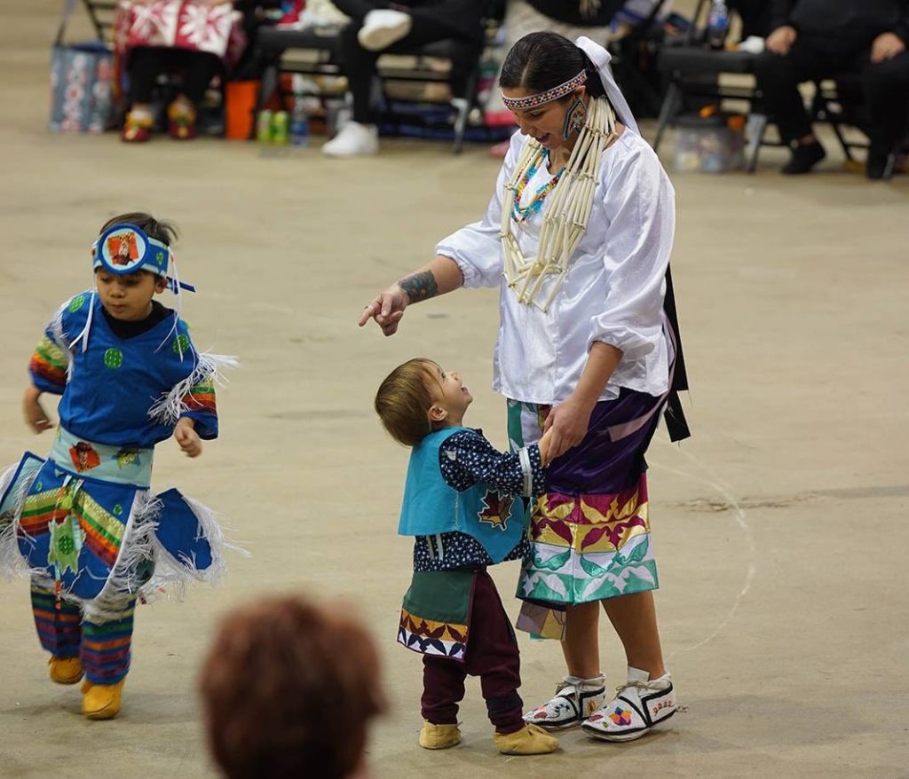 woman and two young boys wearing Native American regalia at a powwow.