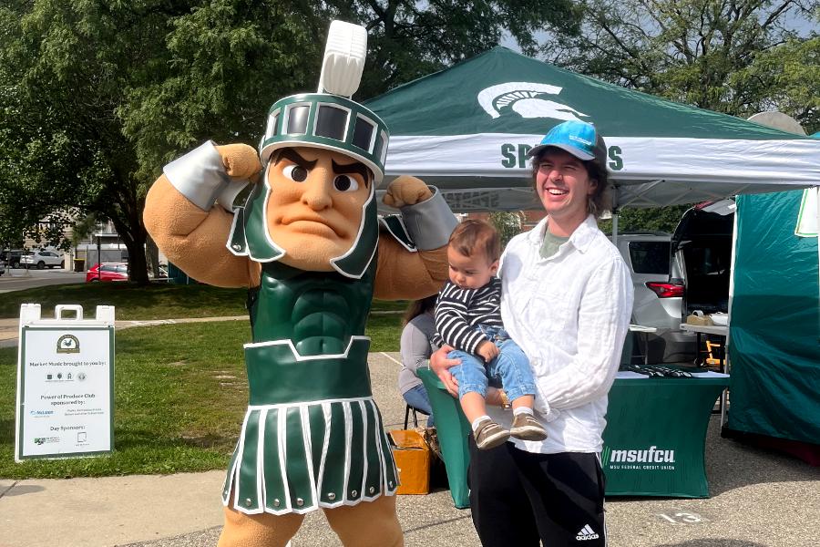 I man holding a baby standing next to a Spartan mascot outdoors.